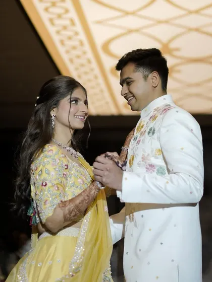 A sweet, interactive moment between the couple. Her makeup is fresh and bright, perfectly suited for a daytime engagement ceremony and complementing her colorful embroidered lehenga.