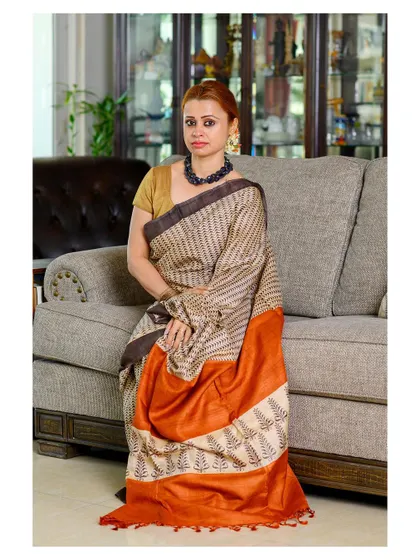 A full-length portrait showcasing a striped tussar silk saree. The indoor home setting gives the image a natural and relatable feel, perfect for a brand that values authenticity.