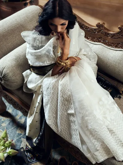 This shot captures a quiet, introspective moment. The soft lighting and elegant pose create a mood of sophisticated grace, highlighting both the texture of the white saree and the ornate gold jewelry.