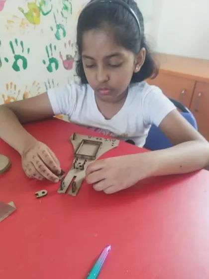 A student carefully organizes and assembles the small parts of a wooden mechanical kit.