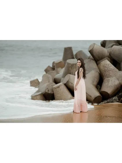 A full-length portrait on the beach, with the waves and sea rocks creating a dramatic natural backdrop. Her pose is elegant and effortless, perfect for a lifestyle or fashion shoot.