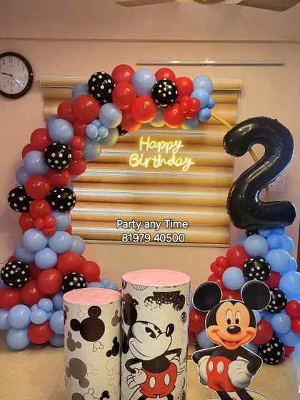A fun Mickey Mouse theme for a 2nd birthday, with a red, blue, and black balloon arch, a Mickey cutout, and themed plinths.