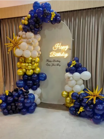 A stylish birthday backdrop with a balloon arrangement in navy blue, white, and gold against a custom arched panel.