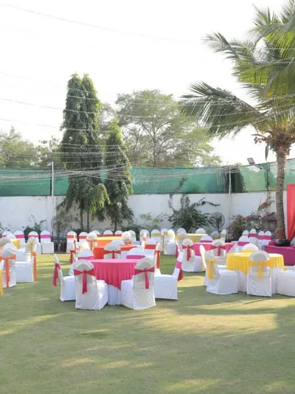 A wide view of an outdoor lawn setup for a Mehendi function. The space is filled with colorful tables and chairs, creating a bright and cheerful atmosphere for the daytime event.
