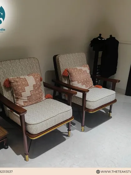 A pair of mid-century inspired lounge chairs with solid teakwood frames and patterned upholstery. The addition of colorful throw pillows with tassels adds a bohemian touch to their classic design.
