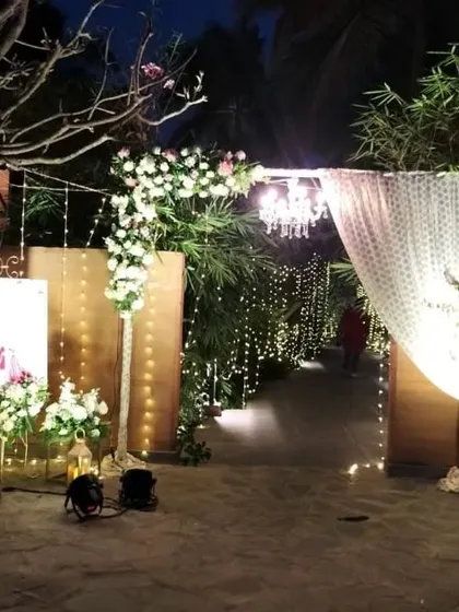 An enchanting entranceway for a Sangeet night. A path lined with fairy lights leads guests through a beautifully draped and floral-adorned archway into the main event area.
