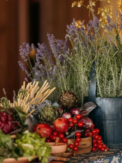 The details of a rustic grazing table. Fresh produce like artichokes, pomegranates, and herbs are used as decor, blending seamlessly with the floral arrangements for an organic, farm-to-table feel.