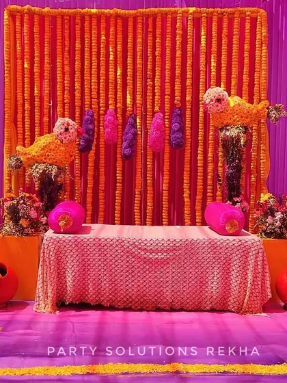 This Haldi seating is a burst of color, featuring a backdrop of marigold strings against a vibrant purple wall. The marigold bird figures add a playful and unique touch to the traditional setup.