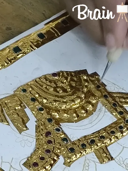 A detailed shot of a student working on the gold relief of a Tanjore painting, using specialized tools to create texture.