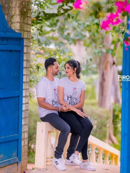 A cute and casual portrait of a couple in matching t-shirts. The bright blue doors and pink flowers add a beautiful pop of color to the scene.