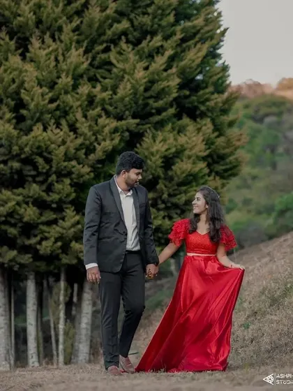 Walking hand-in-hand through a beautiful landscape. The bride-to-be is in a vibrant red satin gown, a classic choice for a romantic and eye-catching pre-wedding look.