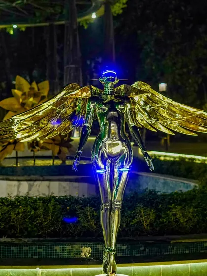 A striking chrome-plated angel statue with golden wings stands as a futuristic and artistic statement piece at a star-studded cocktail affair.