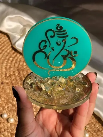 A close-up of a teal-colored mini Ganesha stand. The base is filled with golden flakes, giving it a rich and decorative look. Each one is about 3 inches in size.