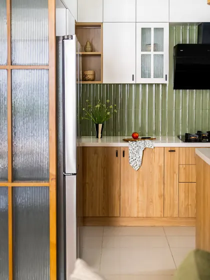This open kitchen features light wooden tones and crisp white surfaces, with a beautiful green-tiled backsplash reminiscent of the countryside. A wood and fluted glass partition cleverly separates the kitchen from the living area while discreetly hiding the fridge.