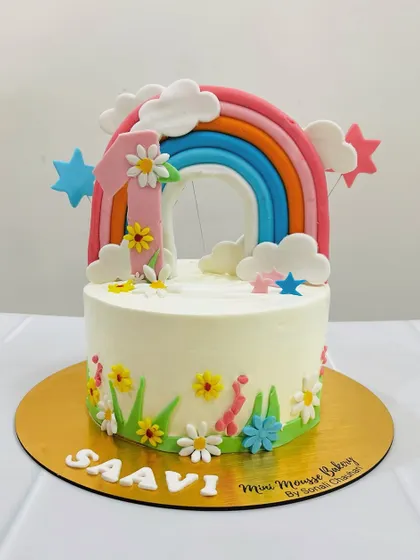 This rainbow-themed cake is all about childhood joy. It features a big, bright rainbow topper, colorful stars, and little flowers, perfect for a vibrant first birthday party.