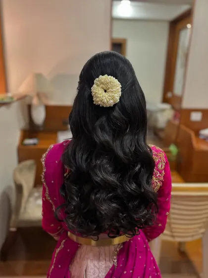A half-up style with voluminous curls, finished with a simple, round jasmine gajra. This combines the beauty of open hair with a traditional touch.