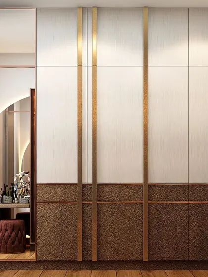 A sophisticated wardrobe design combining white, wood, and textured bronze panels. The vertical brass strips add a touch of linear elegance, and the design includes a seamlessly integrated dressing table nook.