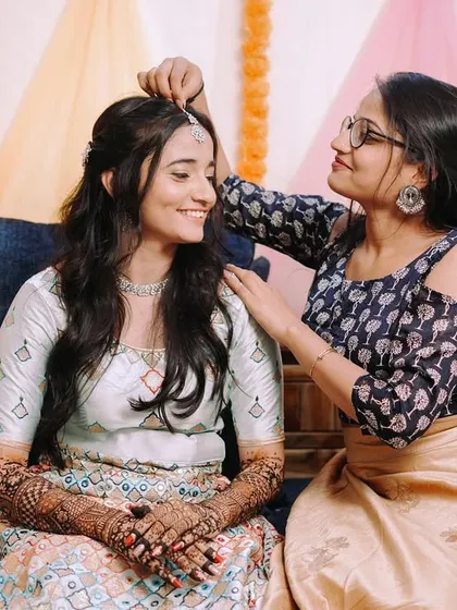 A sweet moment between sisters as one adjusts the maang tikka on the bride during her Mehndi ceremony.
