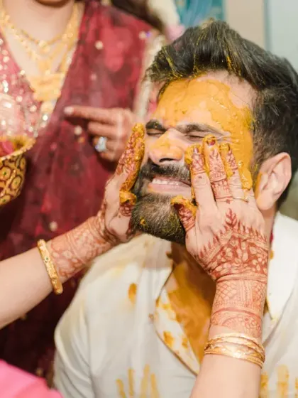 A close-up of the bride's hands applying haldi to the groom's face. This intimate and slightly mischievous moment captures the love and playfulness between the couple.