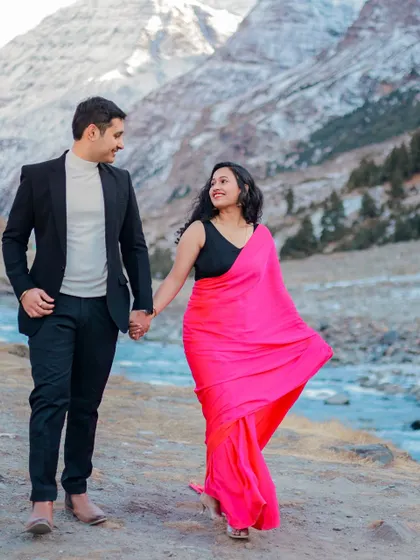 A couple walks hand-in-hand along a riverbank in Himachal, the bride's vibrant pink saree a beautiful contrast to the landscape.