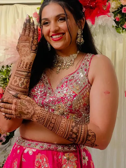 The lovely Raksha, smiling brightly as she shows off her intricate bridal mehendi.