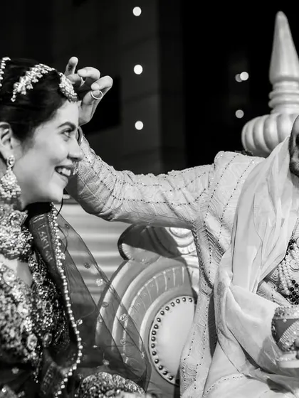 A playful and tender moment at the mandap. The groom gently touches the bride's head, and they share a sweet, knowing smile.