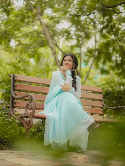 A serene and graceful portrait in a park setting. The natural environment complements the simple elegance of the light blue ethnic suit.