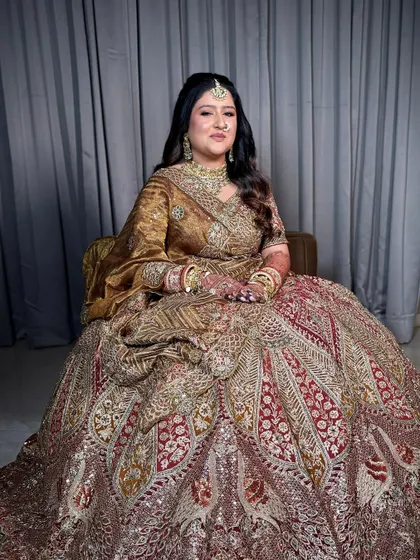 A full-length shot of the bride seated, showcasing the grandeur of her heavily embroidered bridal lehenga.