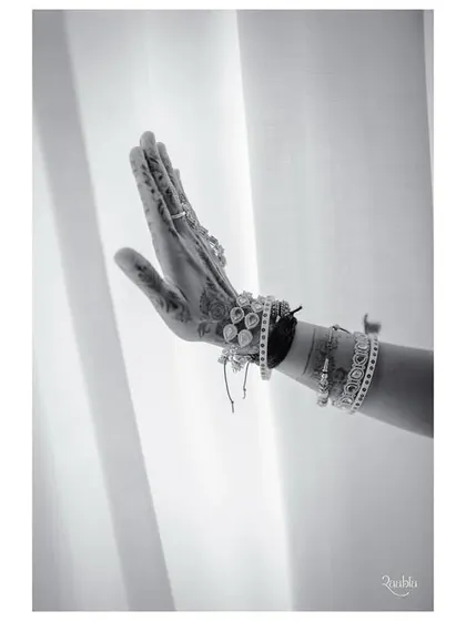 A simple yet powerful black and white image of the bride's hand, adorned with henna and bracelets, against a soft white curtain.