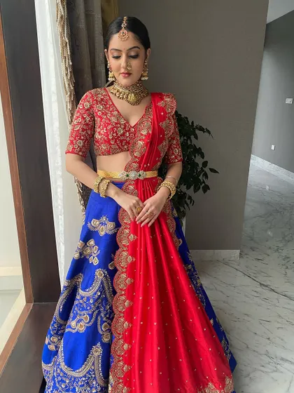 A stunning half-saree look with a vibrant red and blue combination. The makeup is traditional yet glamorous, with a focus on defined eyes.