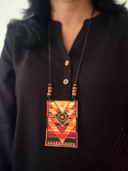 A hand-painted pendant with a striking geometric design in warm, earthy tones. This piece is perfect for adding a touch of tribal-inspired art to any outfit.