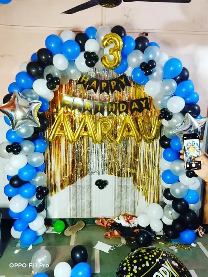 A simple yet stylish birthday decoration at home with a gold and black tinsel curtain and a blue, black, and white balloon arch.