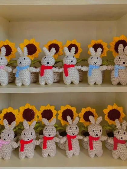 A cute display of my amigurumi bunnies lined up in front of potted sunflowers on my shelf.
