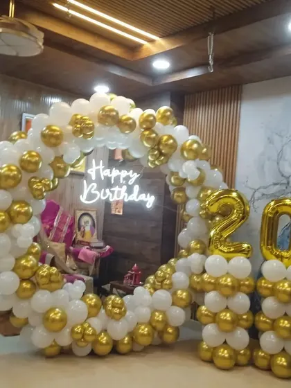 A classic white and gold balloon ring for a 20th birthday. This elegant decoration includes foil number balloons on matching balloon pillars, perfect for a clean and celebratory look.