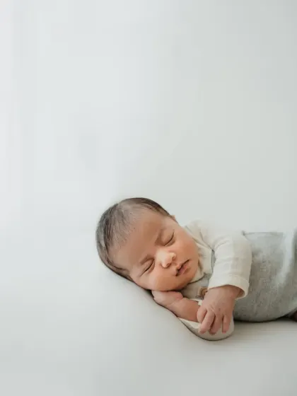 A side profile of a sleeping newborn in a simple grey and white onesie. This minimalist style is perfect for capturing their tiny, perfect form.