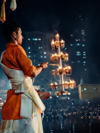 A powerful shot of a priest with the ceremonial lamp, the light illuminating his face against the dark water and city lights.