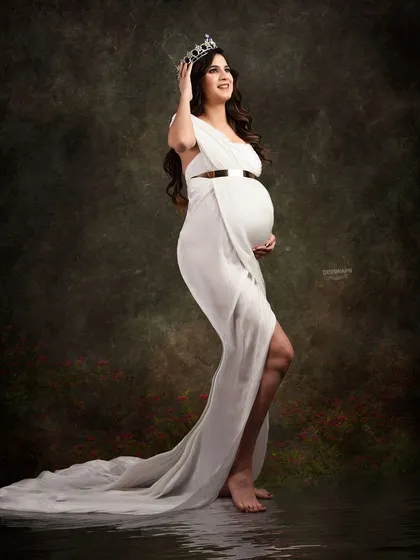 A regal and confident portrait. The client wears a simple white gown and a crown, creating a powerful image of a queen awaiting her heir. The water reflection adds a touch of magic.