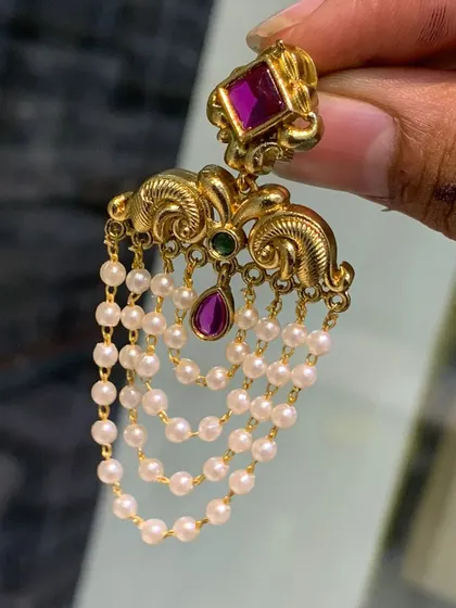 A closer look at these elegant imitation earrings. They are designed to look like traditional gold jewellery, with a ruby-colored stone stud and cascading layers of pearls.