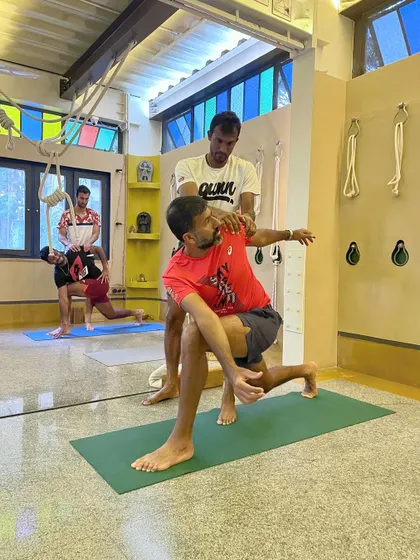 A student assists a professional tennis player in a deep twisting lunge. Partner work is invaluable for athletes to safely explore a greater range of motion and receive feedback on their alignment.