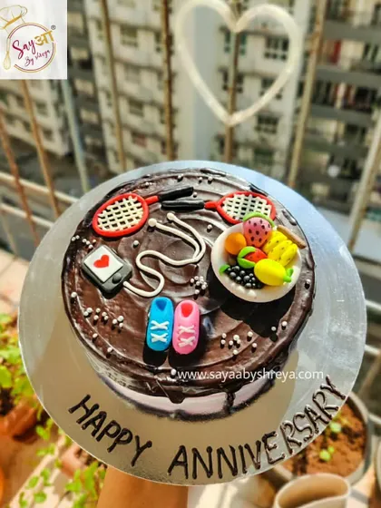An anniversary cake for an active couple. This chocolate cake is topped with fondant decorations representing their shared hobbies, including badminton, fitness, and healthy eating.