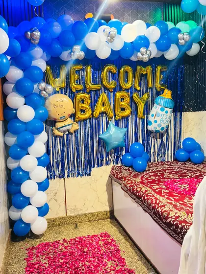 The indoor setup for the 'Welcome Baby' party, featuring a blue and white balloon arch over a blue shimmer curtain and a bed of flower petals.