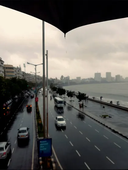 The view of Marine Drive, or the Queen's Necklace, from a foot-over bridge, framed by an umbrella. This classic perspective is made more moody and atmospheric by the rain.