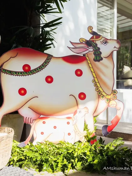 A traditional Pichwai cow cutout stands among fresh greenery, symbolizing prosperity and life, a beautiful element for a baby welcome ceremony.
