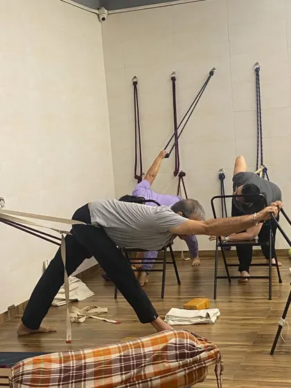 Students using chairs and wall ropes for a supported twisting forward bend. This setup allows for a deep stretch along the side of the body and the hamstrings.