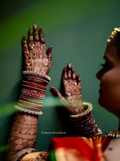 An artistic shot of a bride's hands against a green wall, highlighting the beautiful contrast of the dark henna stain.