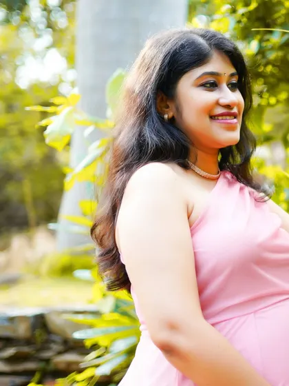 A smiling portrait of the mother-to-be during her outdoor maternity shoot, surrounded by lush greenery.