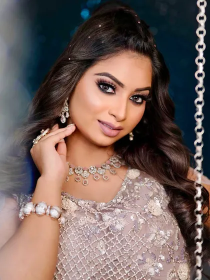 A stunning portrait of a model ready for her sangeet. The makeup features bold, defined eyes and glowing skin, while the hair is styled in a half-updo with delicate pearl accents, a look students practice for their portfolios.
