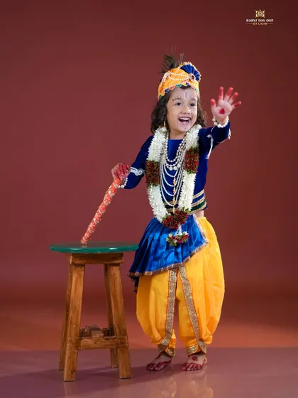 A happy little Krishna waving to the camera. The vibrant costume and joyful expression make this a perfect festive portrait.