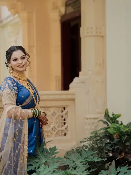 A lovely solo portrait of the bride in her blue Nauvari saree. Posed against a classic building, her confident and happy expression shines through.