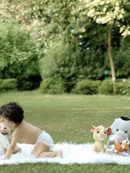 A fun outdoor birthday shoot with a "Hakuna Matata" vibe. The baby crawls on a soft blanket surrounded by his favorite stuffed animals, with bubbles floating in the air.